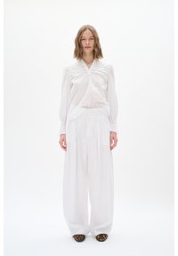 Weiße Bluse mit langen Ärmeln, die über filigrane Ausschnittdetails und einen lockeren Schnitt verfügt, kombiniert mit weiten weißen Hosen und Ballerinas im Leopardenmuster.