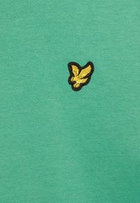 Zielony materiał z małym wyszywanym żółtym ptaszkiem z czarnym obrysem na środku.