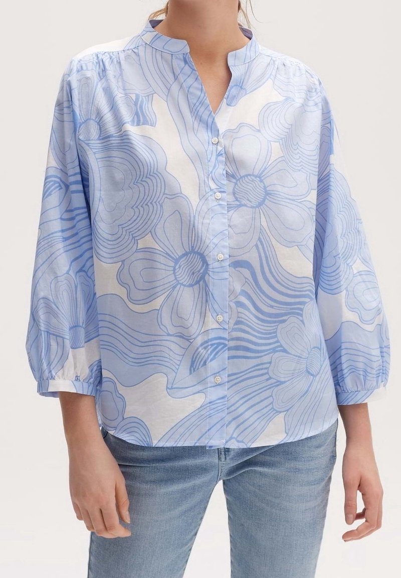 Chemisier bleu clair à motifs floraux, avec des manches bouffantes et un col montant. Fabriqué en tissu doux et aéré.