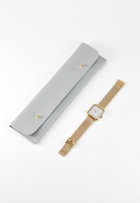 Étui à montre en cuir gris avec fermeture à bouton-pression et une montre avec bracelet en maille accentué en or, présentant un cadran carré blanc.