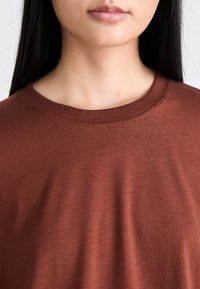 Roestkleurig T-shirt met een ronde halslijn, zachte stof en een relaxte pasvorm. Heeft een gladde textuur en stiksels bij de kraag.