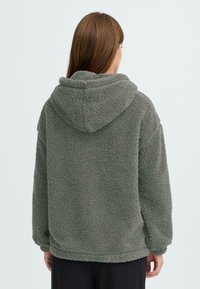 Fleece-Hoodie in dunkelgrün mit weichem und strukturiertem Stoff, oversized Passform und Kapuze. Minimalistisches Design ohne sichtbare Logos.