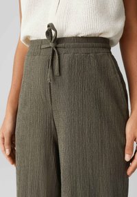 Olivově zelené, strukturované kalhoty s širokými nohavicemi, stahovací gumou v pase a postranními kapsami. Vyrobeno z lehkého, zpruzeného materiálu.