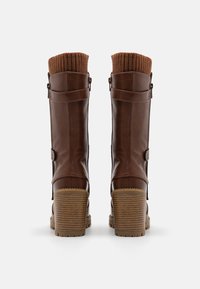 Botas de cuero marrón con un puño de punto acanalado marrón, un tacón grueso y un detalle de hebilla en el costado. Textura suave con una suela apilada.
