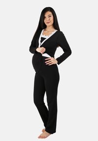 Conjunto de pijama de maternidad en negro con mangas largas, detalles de encaje blanco y un frente drapeado. Tela suave, pantalones ajustados y una silueta relajada.