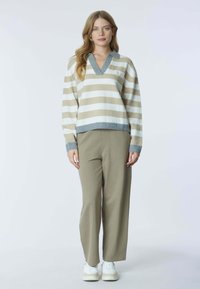 Maglione a righe crema e beige con scollo a V e colletto grigio, abbinato a pantaloni larghi verde oliva e sneakers bianche.