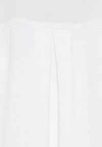 White top featuring a smooth texture, with a horizontal seam and a subtle pleat detail at the neckline. Minimalist design and color.