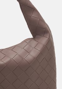 Brązowa włókiennicza skórzana torba na ramię o charakterystycznej teksturowanej powierzchni i zakrzywionym uchwycie, z prostym zapięciem na zamek błyskawiczny.