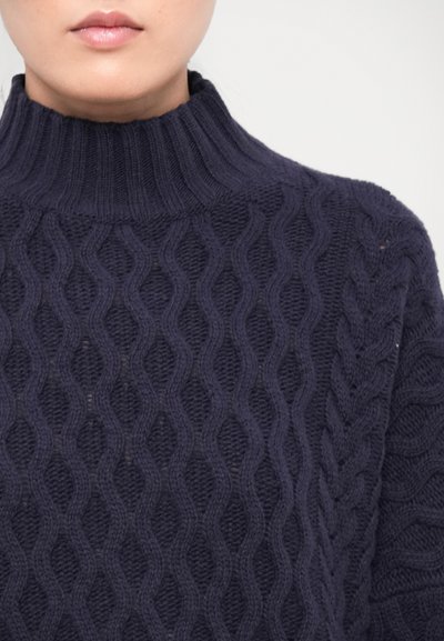 Navy high-neck cable knit sweater with a textured wavy pattern. Ribbed collar, soft wool material, and fitted design.