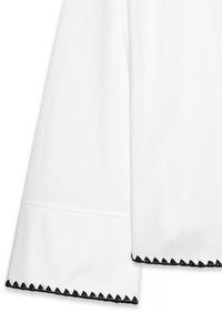 Weißes Baumwollhemd mit langen, weiten Ärmeln, das an den Manschetten mit schwarzem gewelltem Rand verziert ist und minimale Designdetails aufweist.