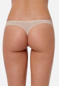 Thong beige translucide avec une taille lisse et une couverture minimale, fabriqué à partir d'un tissu léger et extensible pour le confort et l'ajustement.