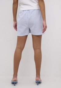 Pantalones cortos a rayas en azul claro y blanco, hechos de una tela con cintura elástica. Llevados con zapatos de tacón azul claro.