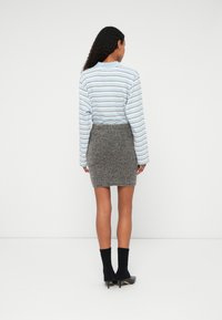 Pitkähihainen sinivalkoraitainen paita, johon on yhdistetty teksturoitu harmaa hame, mustat nilkkasukat ja teräväkärkiset mustat kengät, näkyy takaa.