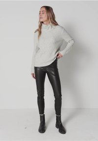 Pull en maille côtelée gris clair avec un col drapé, associé à un pantalon ajusté en simili cuir noir et des bottines noires.