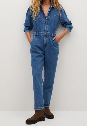 Kombinezon dżinsowy z kołnierzem, długimi rękawami i dwoma przednimi kieszeniami. Posiada luźny krój i zwężane nogawki w średnim odcieniu niebieskiego.