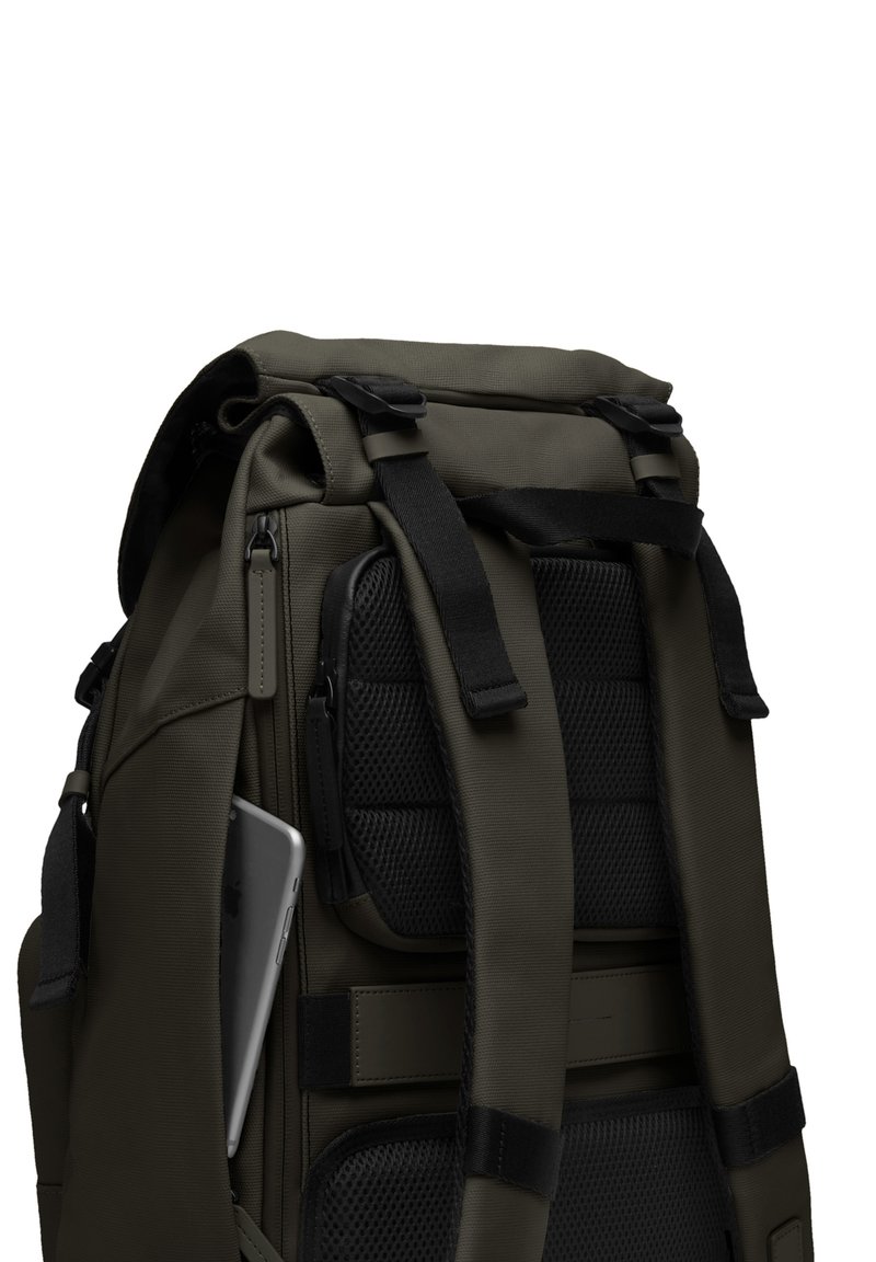 Sac à dos vert foncé avec des bretelles réglables, panneau en maille noire texturée, poche externe et un smartphone gris visible rangé à l'intérieur.