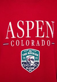 Tessuto rosso con testo bianco "ASPEN COLORADO" e un patch a tema sciistico che mostra uno sciatore, montagne e alberi con "THE ROCKIES" e "ALPINE SKI."