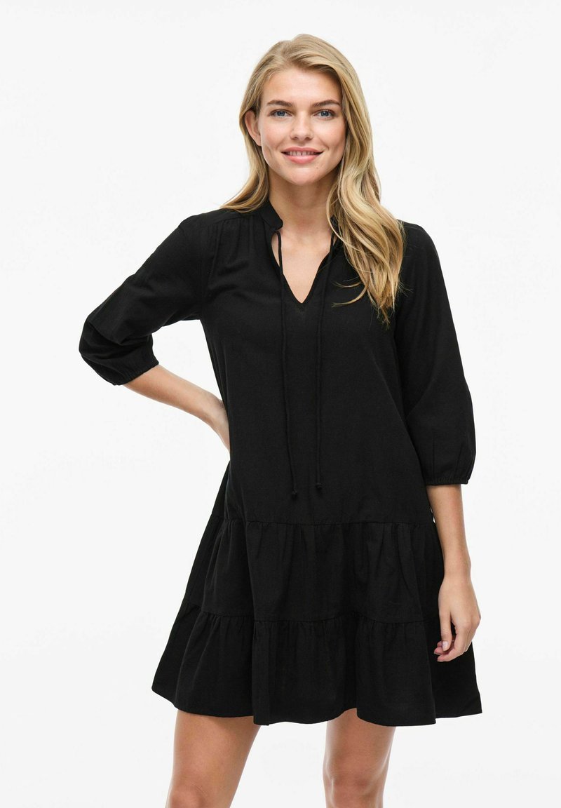 Melnas kokvilnas kleitas ar trim ceturtdaļu piedurknēm, V veida kaklu, savelkamām detaļām un slāņainu volānu apakšmalā. Mīksta virsma un brīva piegriezuma.