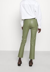 Zielone spodnie z sztucznej skóry w stylu dzwonów o gładkiej fakturze, z detalami na szwie z tyłu i lekko błyszczącym wykończeniu. W zestawieniu z białą, krótką koszulą.