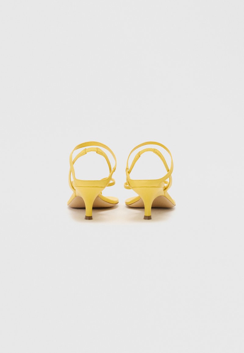Yellow heeled sandals with a smooth texture, open back design, thin straps, and a small, structured heel.