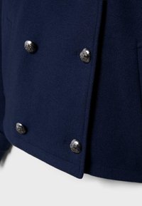 Laivastonsininen villakangastakki, jossa tuplarivinen malli, hopeiset koristeelliset napit ja pehmeä, teksturoitu pinta.