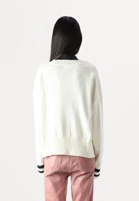 Maglione bianco a maglia con orlo e polsini a coste; presenta una vestibilità comoda e un design a girocollo. Indossato con pantaloni in velluto a coste rosa.