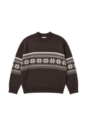 Homme portant un pull en maille foncé à motifs et une casquette de baseball verte, tenant une veste marron avec une doublure en fourrure blanche sur l'épaule.