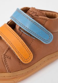 Braunes Leder-Shoe mit orangefarbenen und blauen Klettverschlüssen. Abgerundete Spitze, strukturiert Oberfläche und einer weichen Innenausstattung für Komfort.