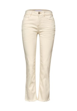 Nahaufnahme einer Person, die cremefarbene Jeans aus Denim trägt, zeigt die Gesäßtaschen und ein goldenes Armband am rechten Handgelenk.