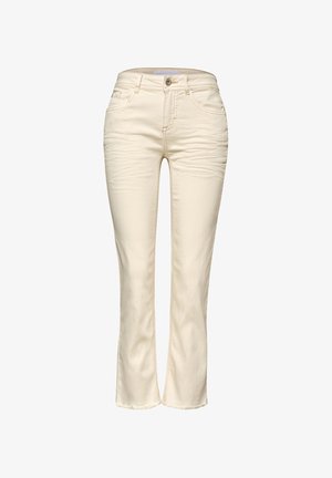 Nærbillede af person iført cremefarvede denimjeans, viser baglommerne og et guldbånd på højre håndled.