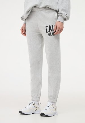 Pantaloni sportivi grigi con vita elasticizzata, caviglie a costina e stampa nera "CALIFORNIA BEL-AIR" sulla coscia sinistra. Texture del tessuto morbida.
