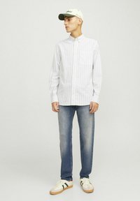 Camisa de cuadros en blanco y azul claro, combinada con vaqueros azul y zapatillas casuales. Gorra verde con detalle de logo.