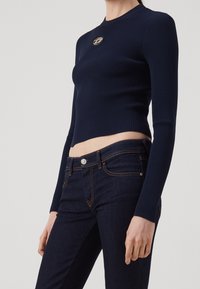 Mörkblå, ribbad långärmad topp med en cropped design och en metallisk logodetalj på bröstet, tillsammans med mörkblå figurnära jeans.
