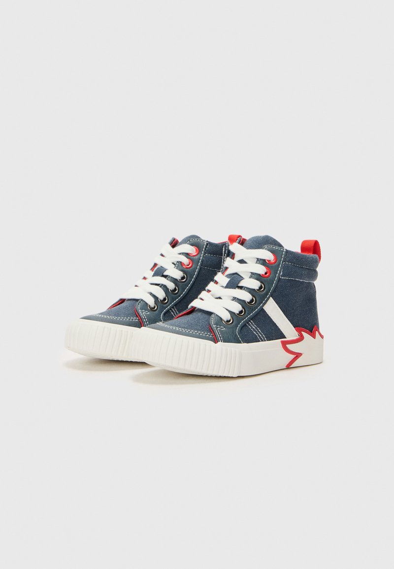 Baskets montantes en denim bleu foncé avec des lacets blancs, des accents rouges et une semelle en caoutchouc blanche et rouge distinctive. Dispose d'un col rembourré.