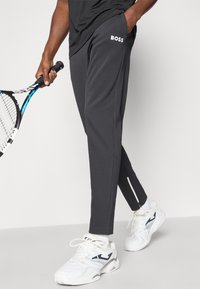 Σκούρο γκρι αθλητικά παντελόνια με το λογότυπο "BOSS" στην αριστερή τσέπη, με φερμουάρ στα τελειώματα. Συνδυασμένα με λευκά αθλητικά παπούτσια.