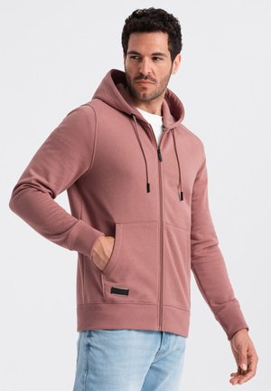 Pink zip-up hoodie made of soft fabric, featuring a drawstring hood, front pockets, and ribbed cuffs. Notable black hardware accent.