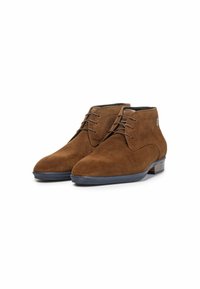 Bottines en daim marron avec un bout arrondi, un laçage, et une finition texturée. Dotées d'une semelle en caoutchouc bleu foncé et basse.