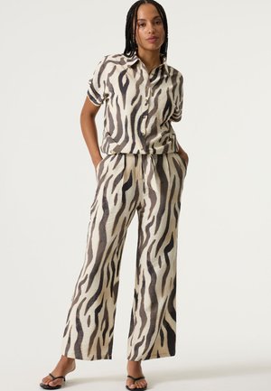 Zweiteiliger Anzug bestehend aus einem kurzärmligen Hemd mit Knöpfen und einer weit geschnittenen Hose, in cremefarbenem Grundton mit braunen und schwarzen abstrakten Streifenmustern.