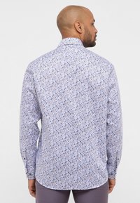 Camicia a stampa floreale in azzurro chiaro con piccoli fiori viola e bianchi. Maniche lunghe, colletto classico e polsini con bottoni. Materiale in cotone.