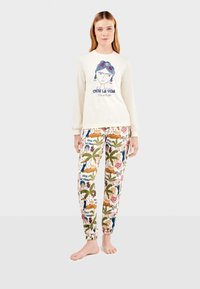 Witte blouse met lange mouwen en een blauw grafisch ontwerp. Gecombineerd met kleurrijke patroonbroek met bloemen- en palmontwerpen.