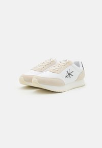 Sneaker sintetiche bianche con accenti in suede beige, punta rotonda, design con lacci e dettaglio del logo sul lato. Suola testurizzata per una buona aderenza.