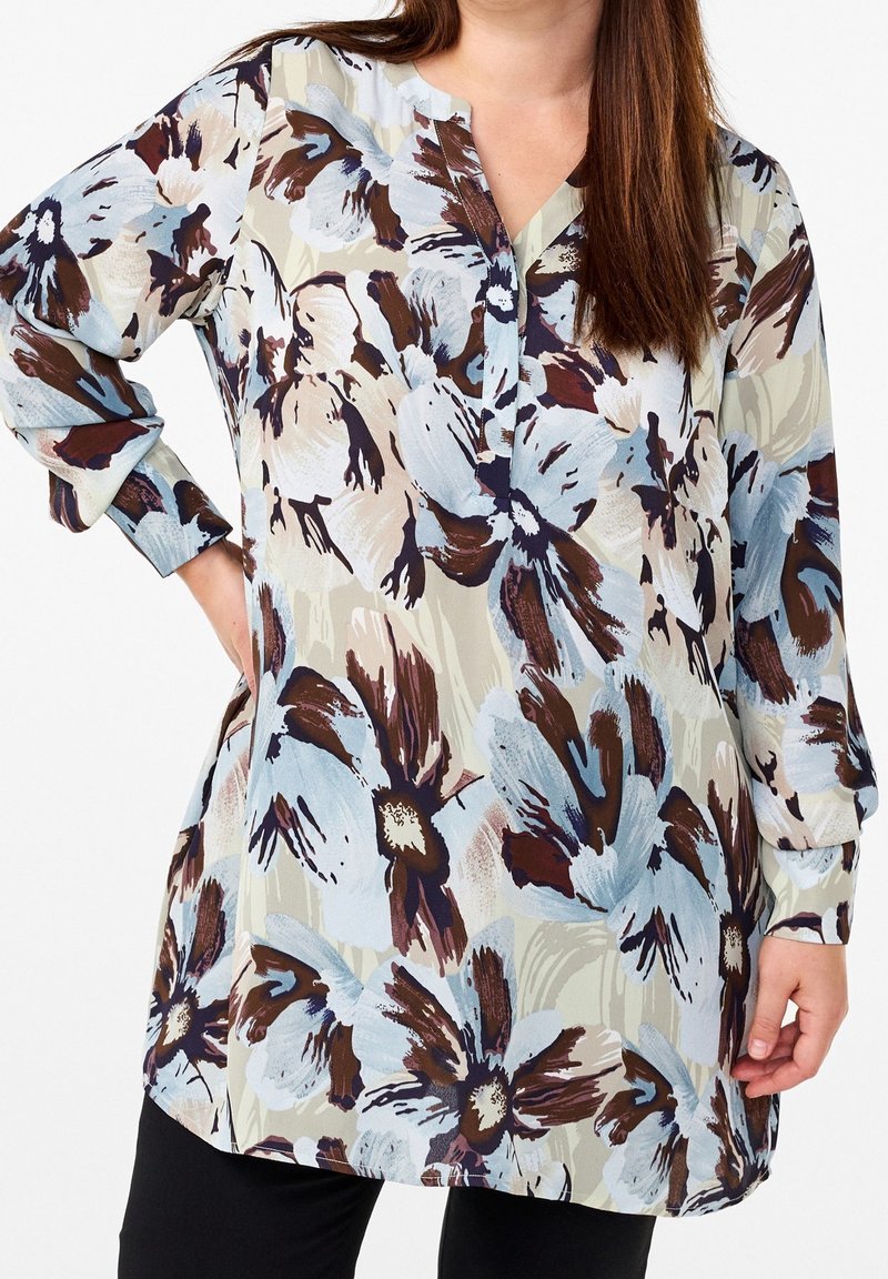 Lange, bloemenblouse in lichte tinten met grote blauwe en bruine bloemen op een crèmekleurige achtergrond. Inclusief een kraag en een knoopsluiting aan de voorkant.