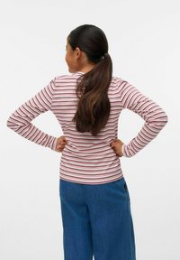 Camicia a maniche lunghe bianca con strisce rosse, caratterizzata da un design aderente e texture a coste, abbinata a jeans a gamba larga blu.