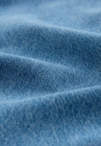 Denimstoff in Hellblau, mit glatter Textur, feinen Webarten und subtilen Farb- und Schattierungsvariationen.