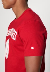 T-shirt in cotone rosso con grafica "Stanford" in bianco, colli rotondo e maniche corte. Il logo è visibile sulla manica.