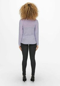 Gehaakte trui in een verloop van lavendel tinten, met lange mouwen, gecombineerd met een zwarte skinny jeans en hoge hakken, gezien vanaf de achterkant.