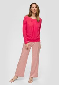 Langärmliges Oberteil mit Rundhalsausschnitt in leuchtendem Pink, kombiniert mit weit geschnittenen, hellrosa Satin-Hosen. Einfaches Design mit Raffung am Ausschnitt.
