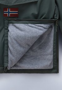 Groene geïsoleerde jas met een rood en blauw Noors vlagpatch. Geopend, met zachte grijze fleece voering zichtbaar in de zak.
