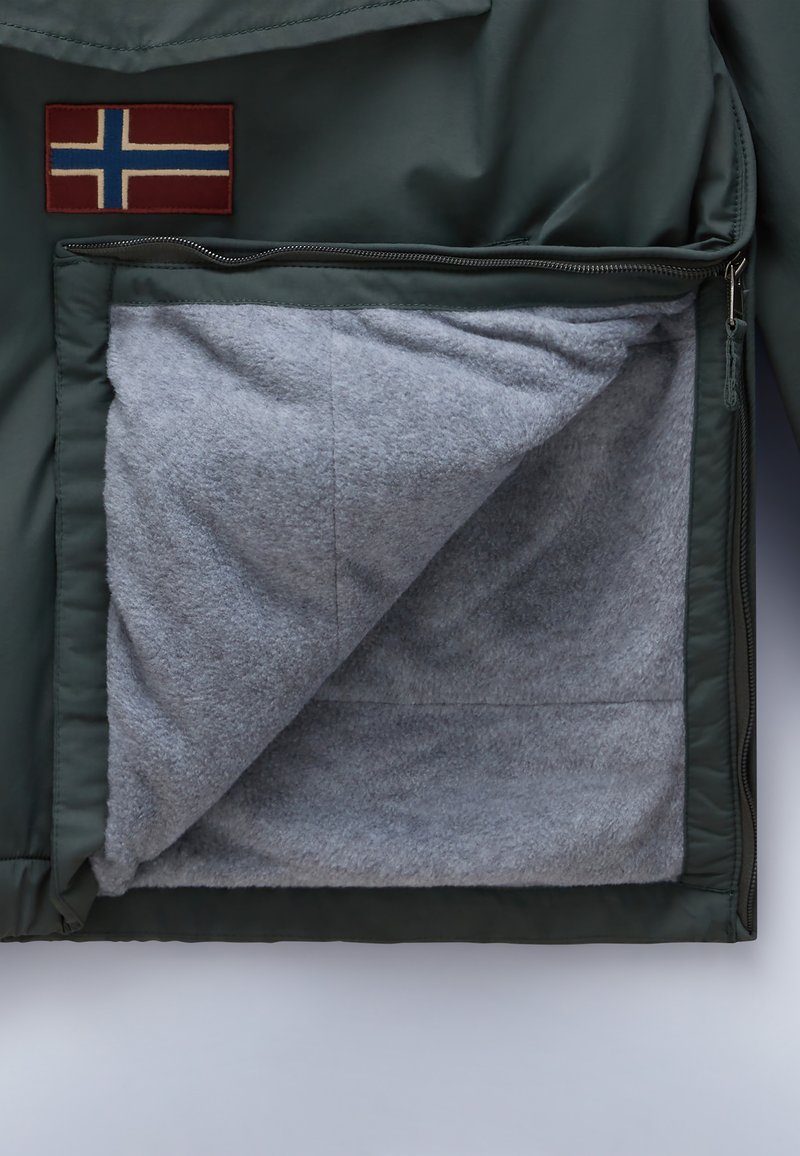 Giacca isolante verde con una toppa a forma di bandiera norvegese rossa e blu. Aperta, rivela un morbido rivestimento in fleece grigio all'interno della tasca.