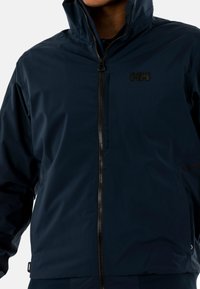 Chaqueta impermeable de color navy, hecha de un material sintético suave, con cremallera frontal, cuello alto y un discreto logo en el pecho.